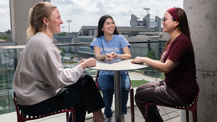 Three Missouri State students sitting at a round table smiling and talking.