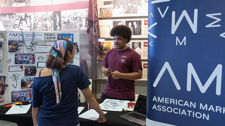 Missouri State student at the American Marketing Association booth talking to a student. 