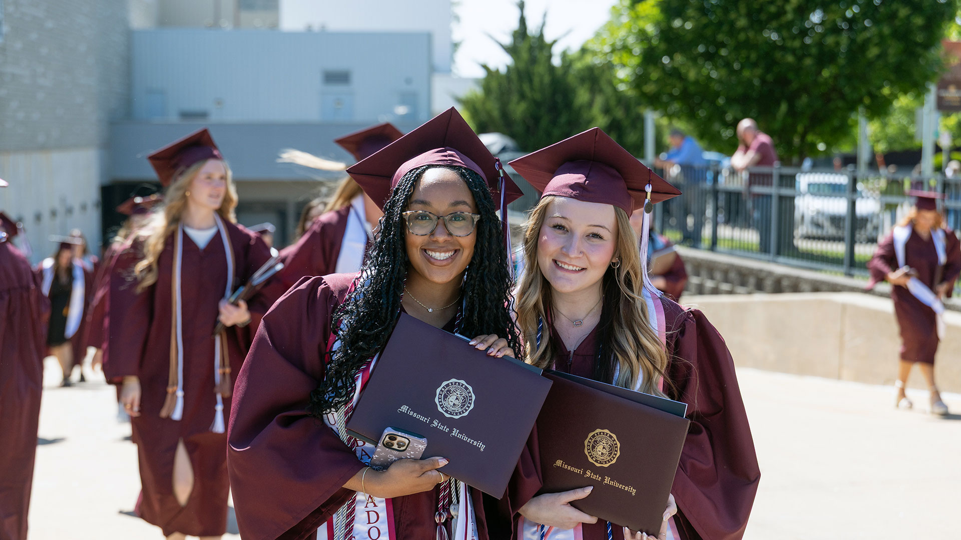 Two Missouri State graduates in cap and gown smiling with their diplomas.