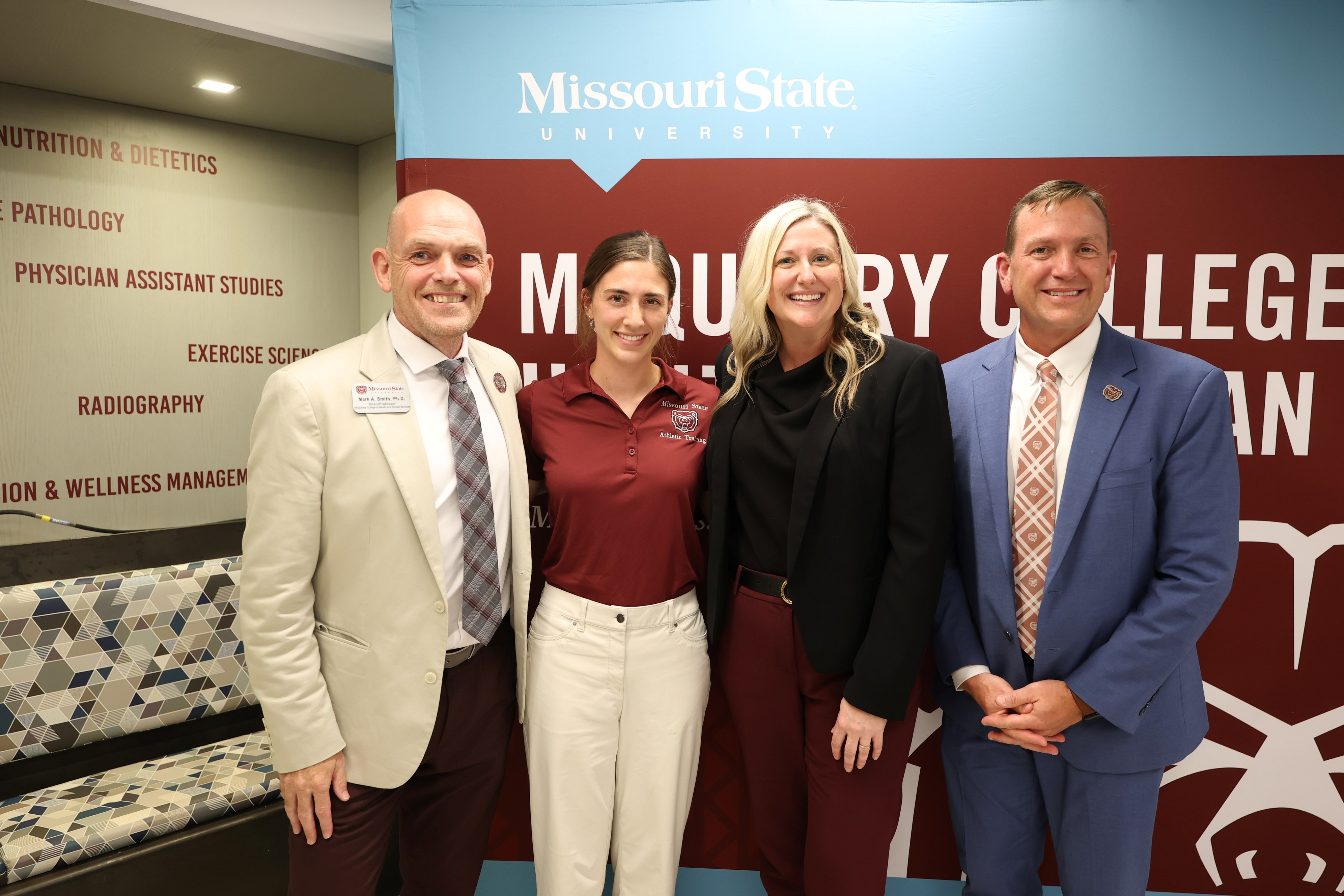 Four people pose together in front of a Missouri State University McQueary College of Health and Human Services backdrop during an event.
