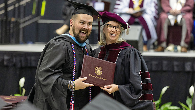Faculty member standing next to a graduate student at commencement for a photo.