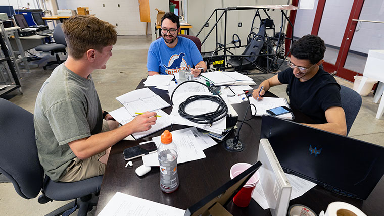 Three Missouri State students sitting at a table filled with paperwork.