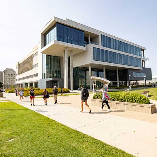 Students walking in front of Glass Hall on a sunny day.