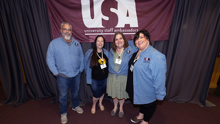 Staff members standing in front of the USA banner on graduation day. 