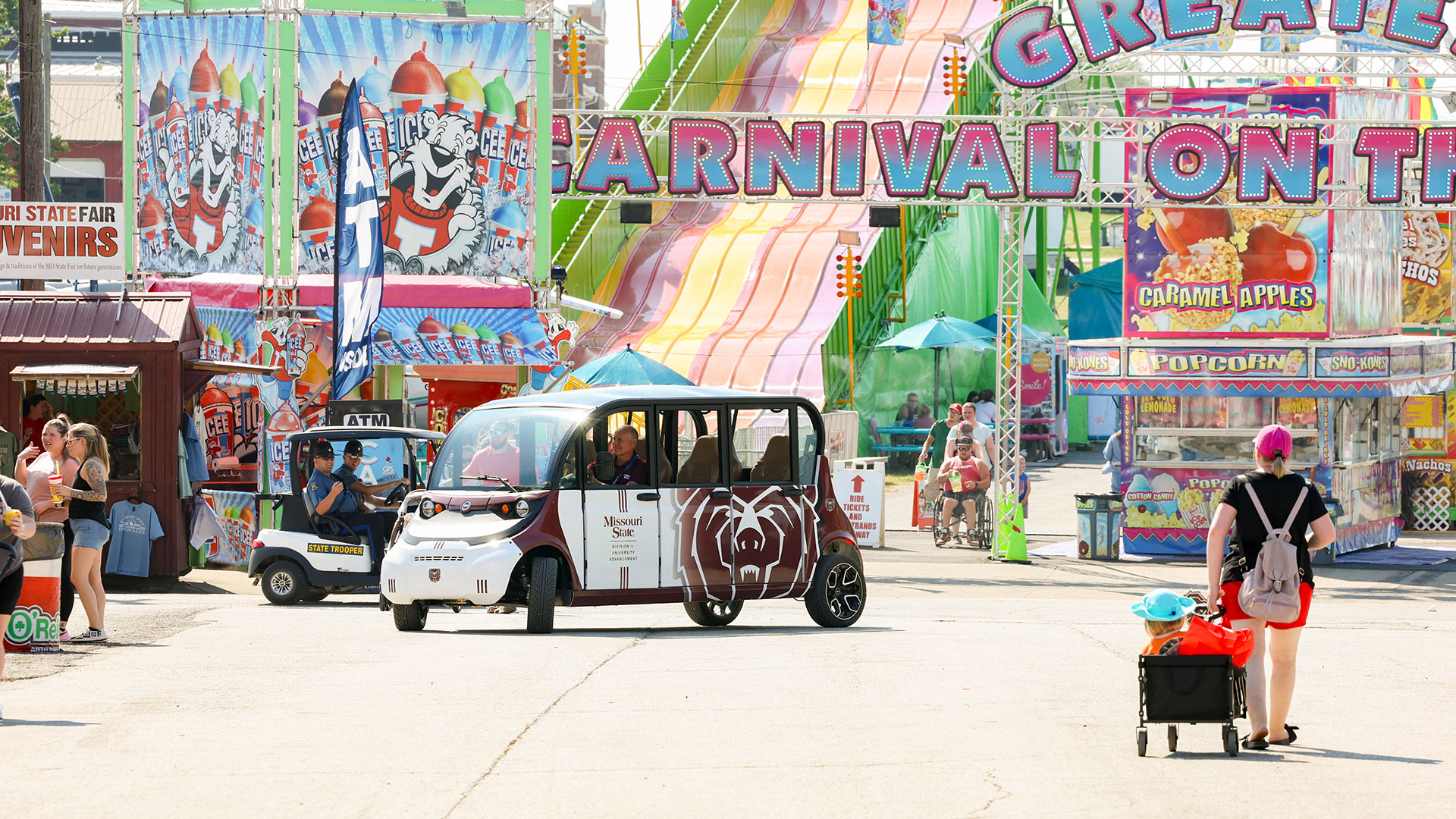 A view of a Missouri State vehicle in front of carnival rides and vendors for food, drinks, and souvenirs.