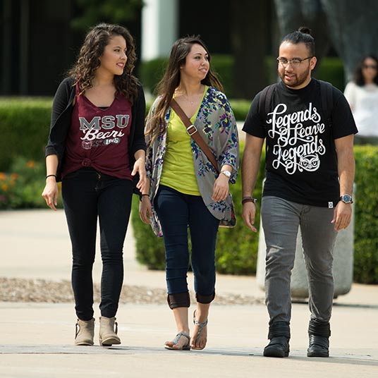 Three students having a chat as they walk to class on campus.