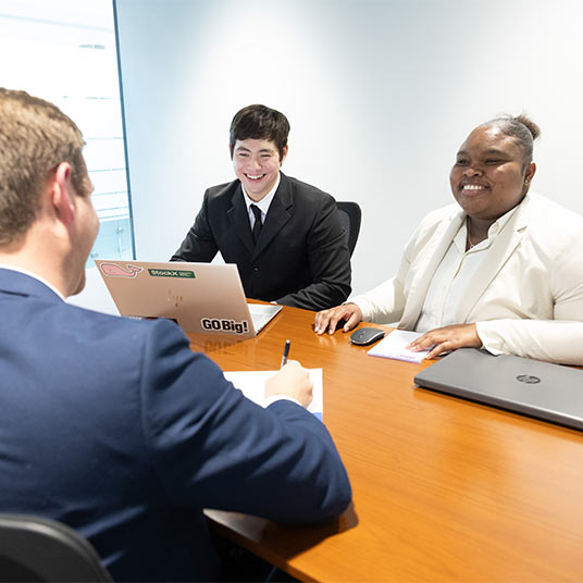 Three professionals having a discussion at a table. One has a laptop open.