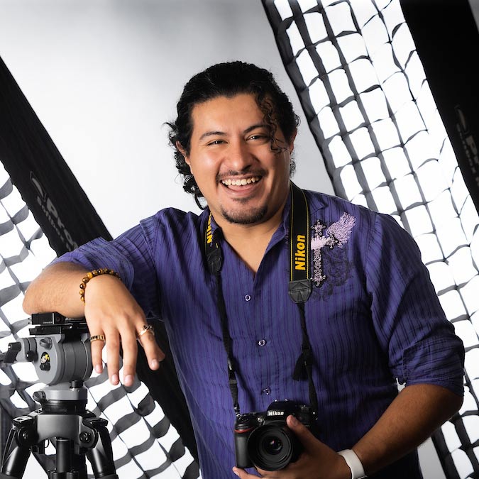 Gio Canales-Rueda Gio Canales-Rueda, a TV production film major at Missouri State. He's wearing a camera around his neck and he's resting his right arm on a tripod.