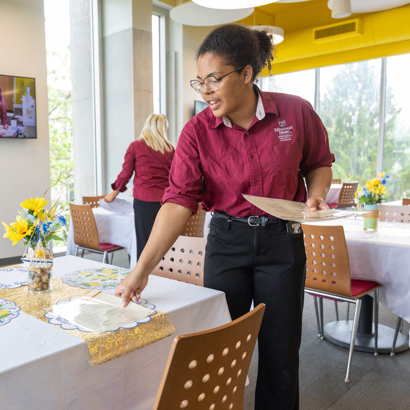 A hospitality student-worker at Carrie's Café sets a table with menus.