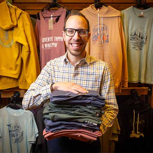 Dr. Josh Coleman, associate professor of marketing, holds a stack of colorful T-shirts in a local store.