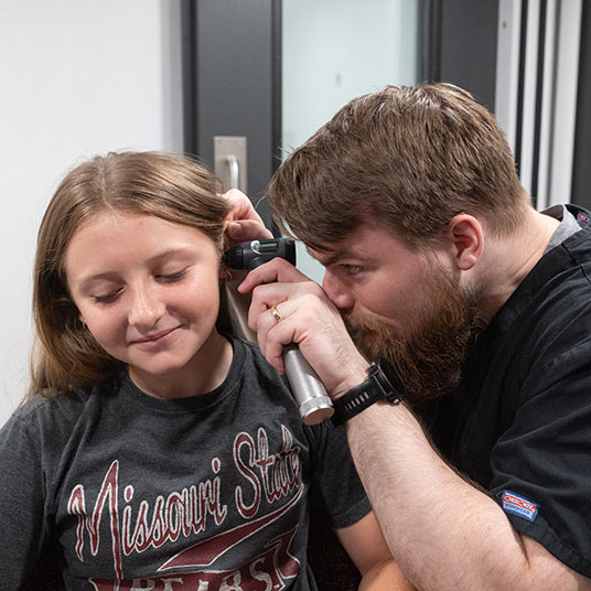 A clinician uses an otoscope to look into his patient's ear.