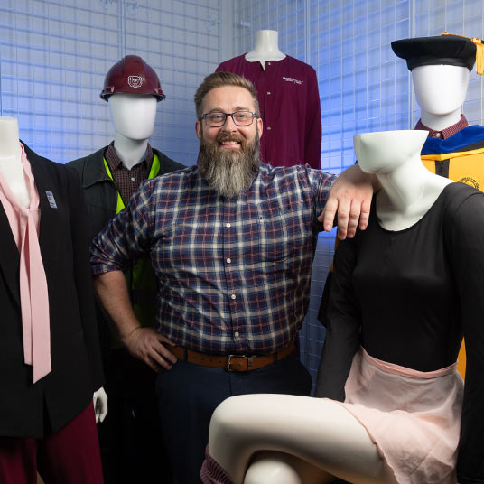 Dr. Daniel Goering, an associate professor in Missouri State's Department of Management, poses next to mannequins that are wearing various kinds of work attire.