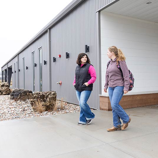 Two agriculture students chat with each other outside a College of Agriculture building.