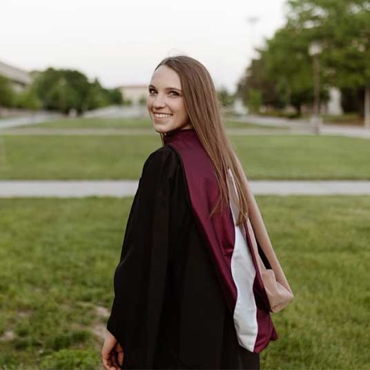 Kennedy Keller, a graduate of the economics program, wearing her commencement gown outside of Strong Hall.