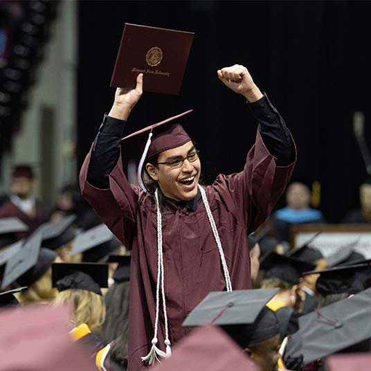 A graduating student holding a diploma during commencement.