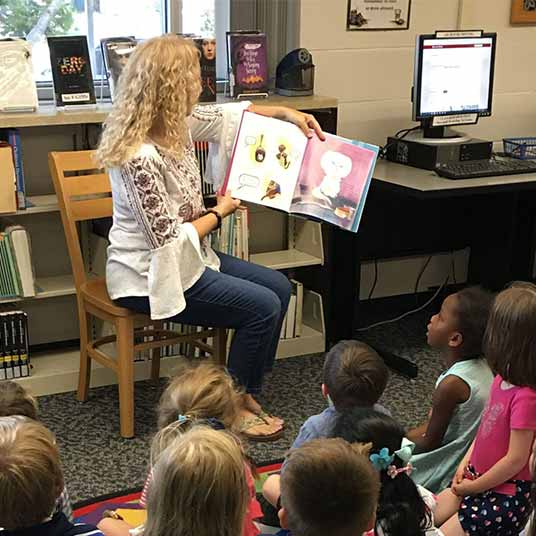 A teacher reads a book to a group of elementary students.