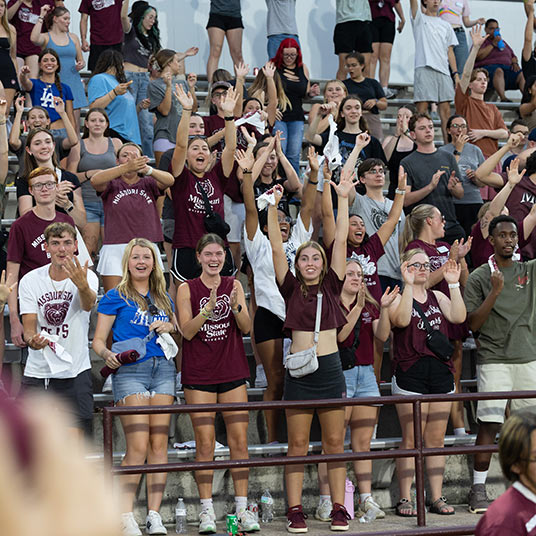 A crowd of students cheer in the stands during an athletic event.