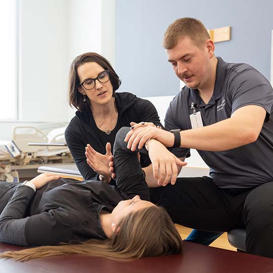 An occupational therapy professors guides two students on treatment techniques.