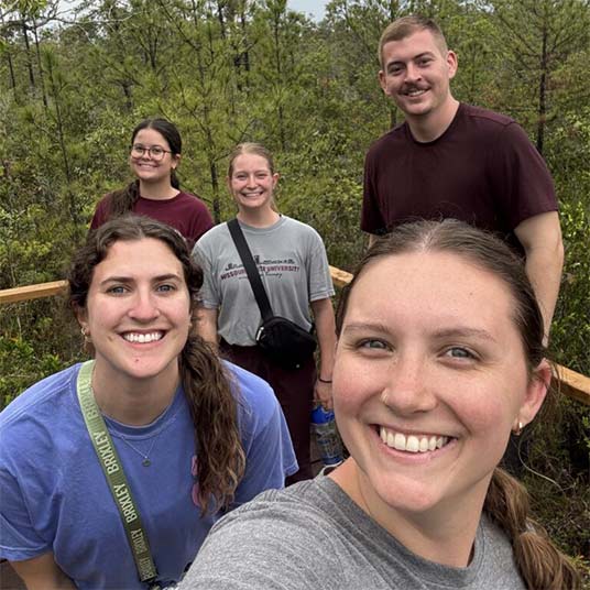 Maci Wilson, an occupational therapy student, and four of her classmates pause for a picture in front of a forest in Belize.