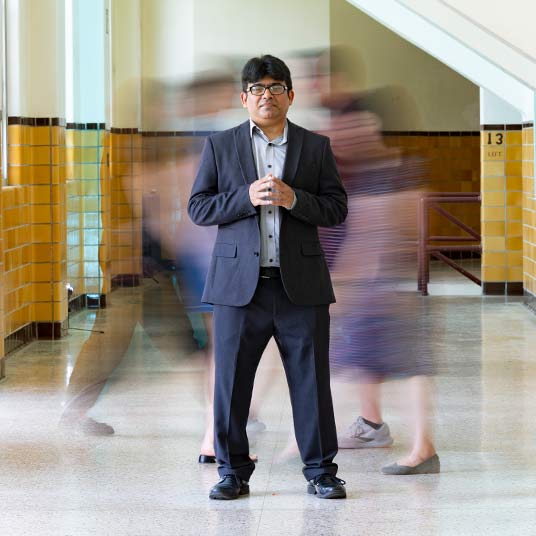 Dr. Muhammad Hassan Raza, an associate professor in the School of Teaching, Learning and Developmental Sciences at Missouri State, stands in the middle of a hallway, with blurry movement behind him.