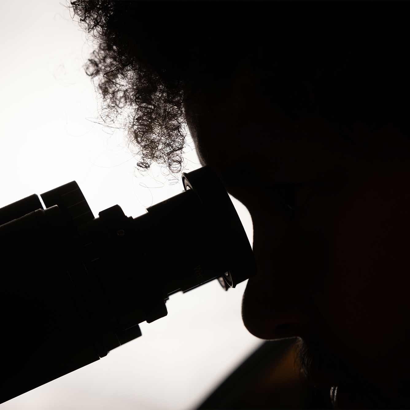 The silhouette of a person looking through a microscope.