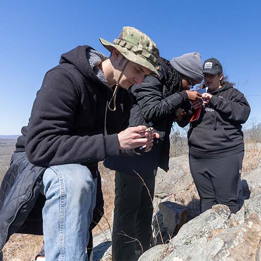 Three geology students examine rock samples at a dig site.