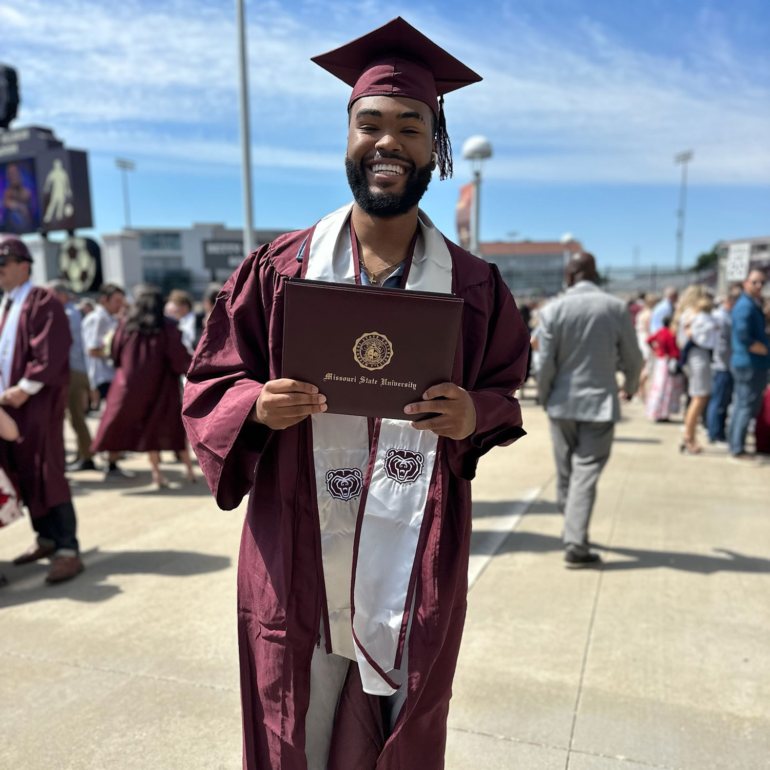 Carly Hendrickson Rodell Andrews, a general studies major, holds up his diploma while donning his graduation regalia after his commencement ceremony.