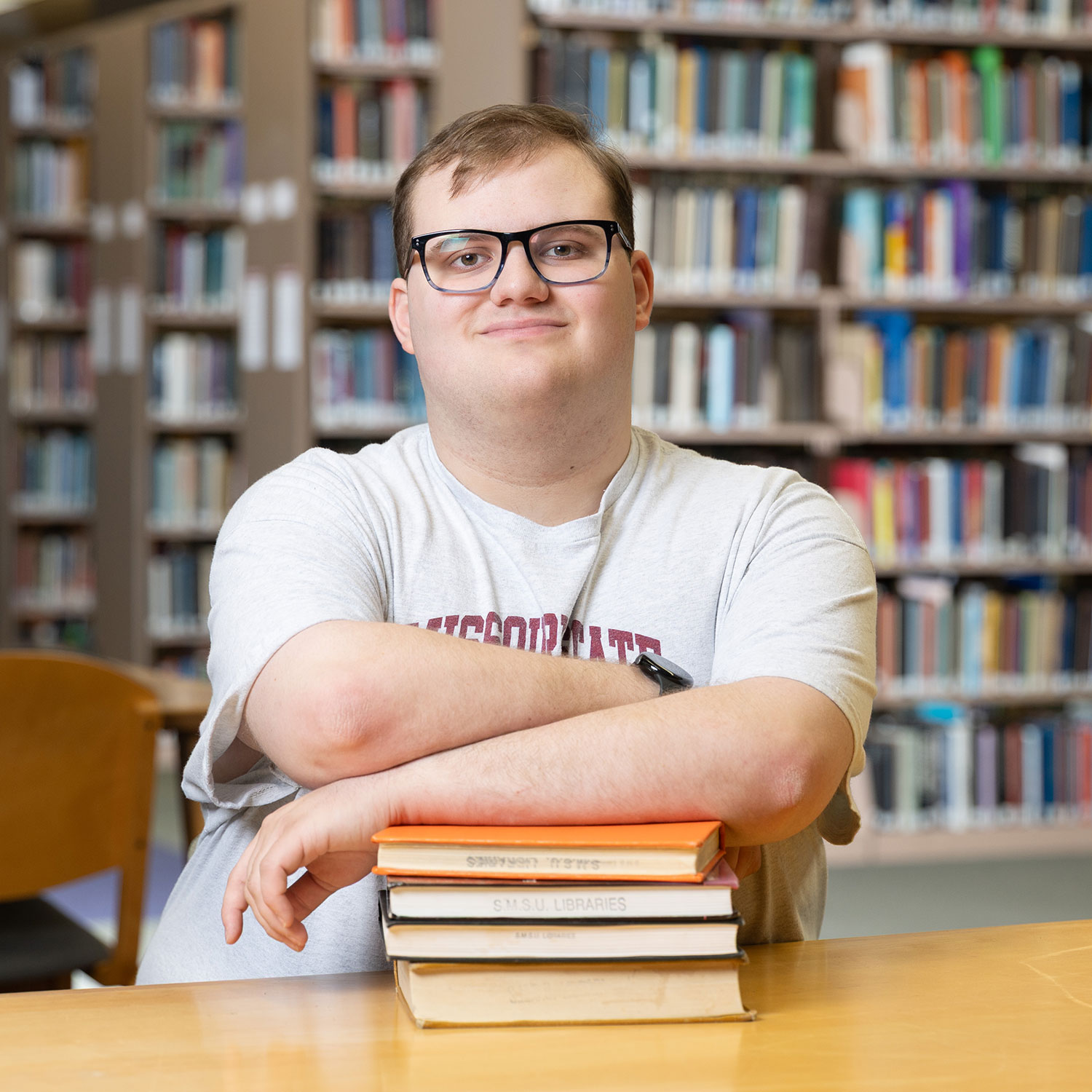 Joseeduardo Granados Rodriguez Daniel Paige, a literature major, is seated at a table in Meyer Library with his arms crossed over a stack of books.