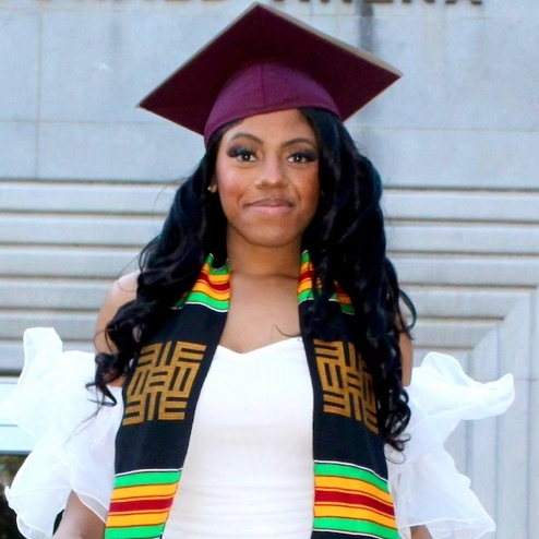 Tylea Wilson wearing a white dress with maroon mortarboard and Kente scarf.