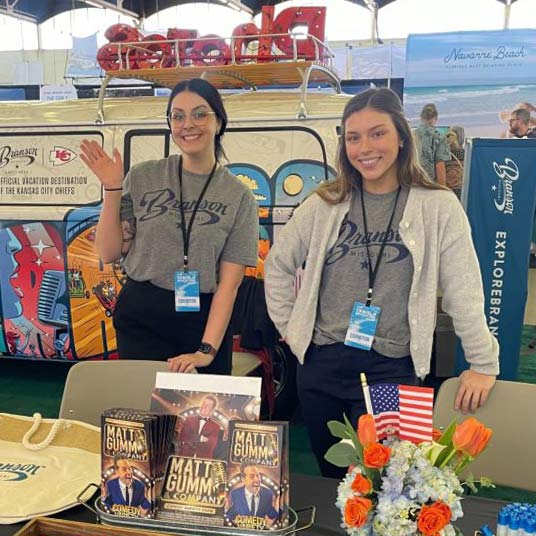 Two Visit Branson employees supervise a booth to promote events and inform tourists about Branson's attractions. The employee on the left is Joslyn Schott, a Missouri State alumna in the hospitality leadership program.