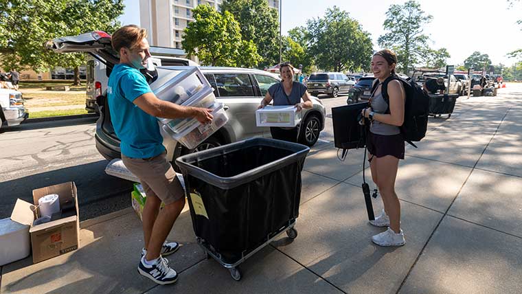 Bear Crew worker helping a student and her parent unload supplies from a vehicle during move-in.