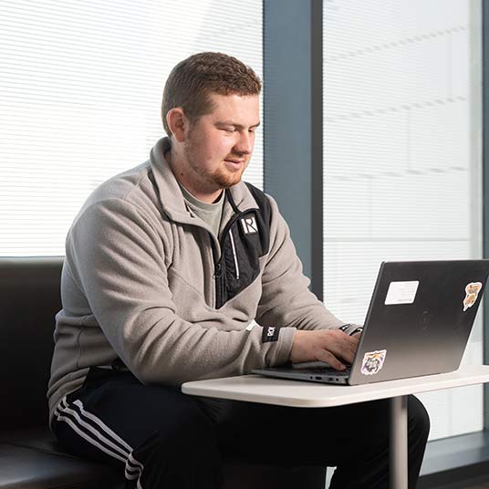 A graduate student types on his laptop.