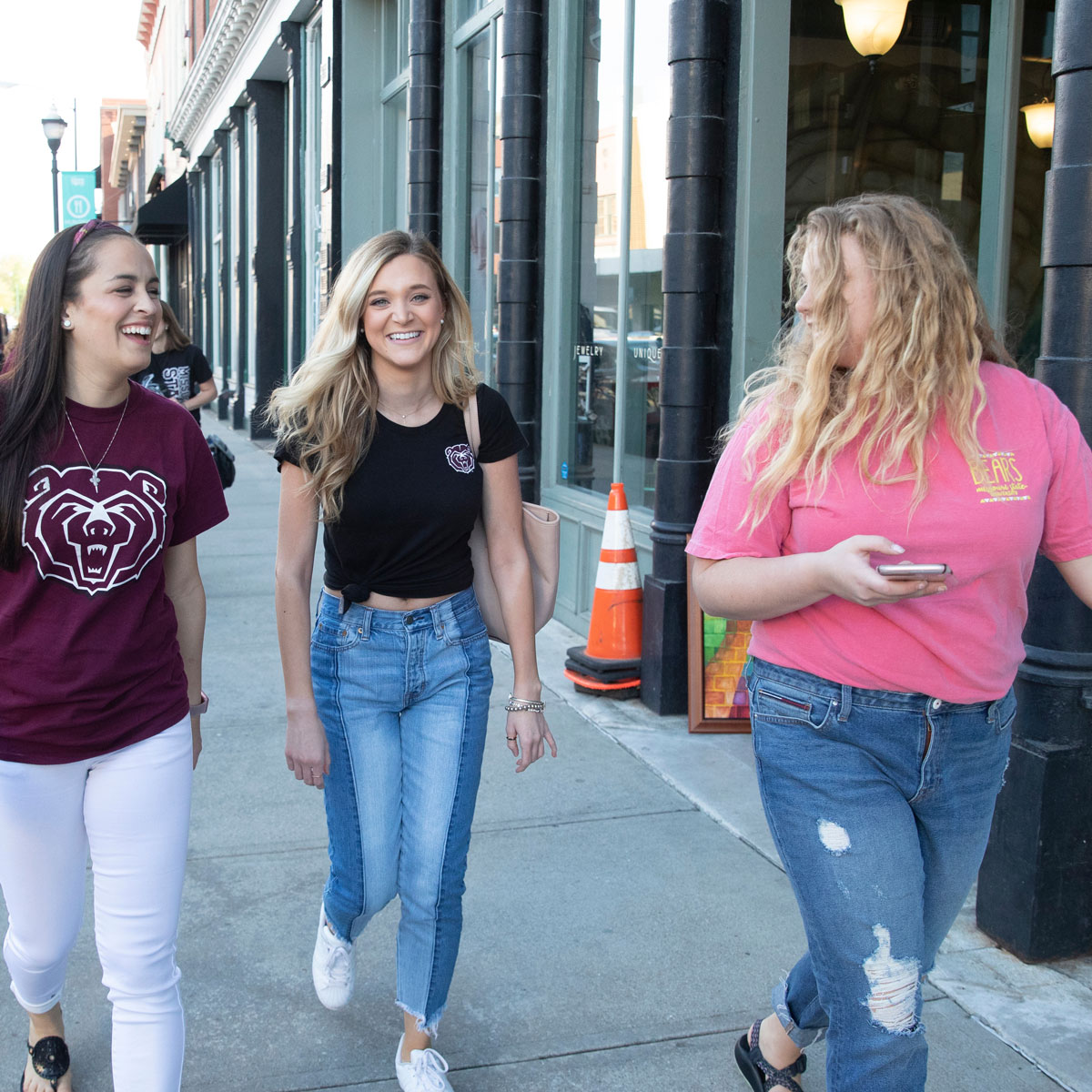Three female students laugh as they walk downtown.