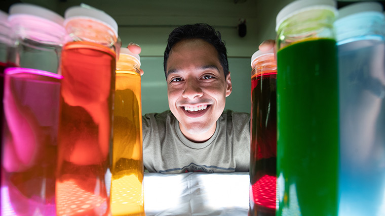 A Missouri State student standing behind beakers containing colorful solution