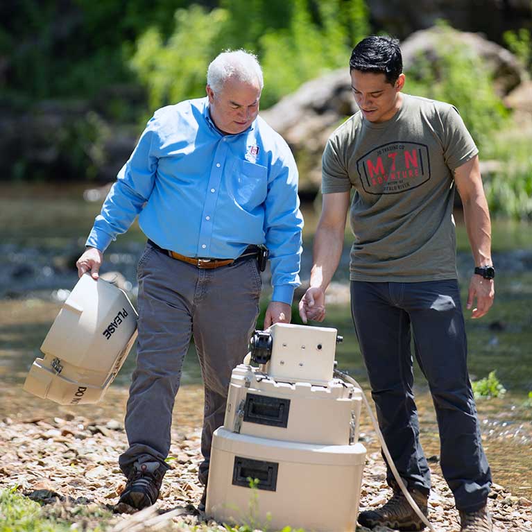 A Missouri State professor and student doing research alongside a creek