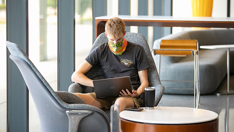 A student sitting in the library looking at his laptop
