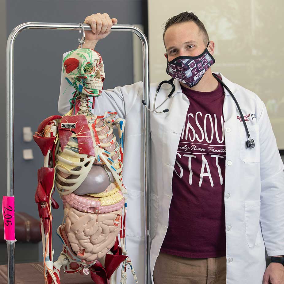 A Missouri State nursing student standing next to an anatomy lab skeleton. 