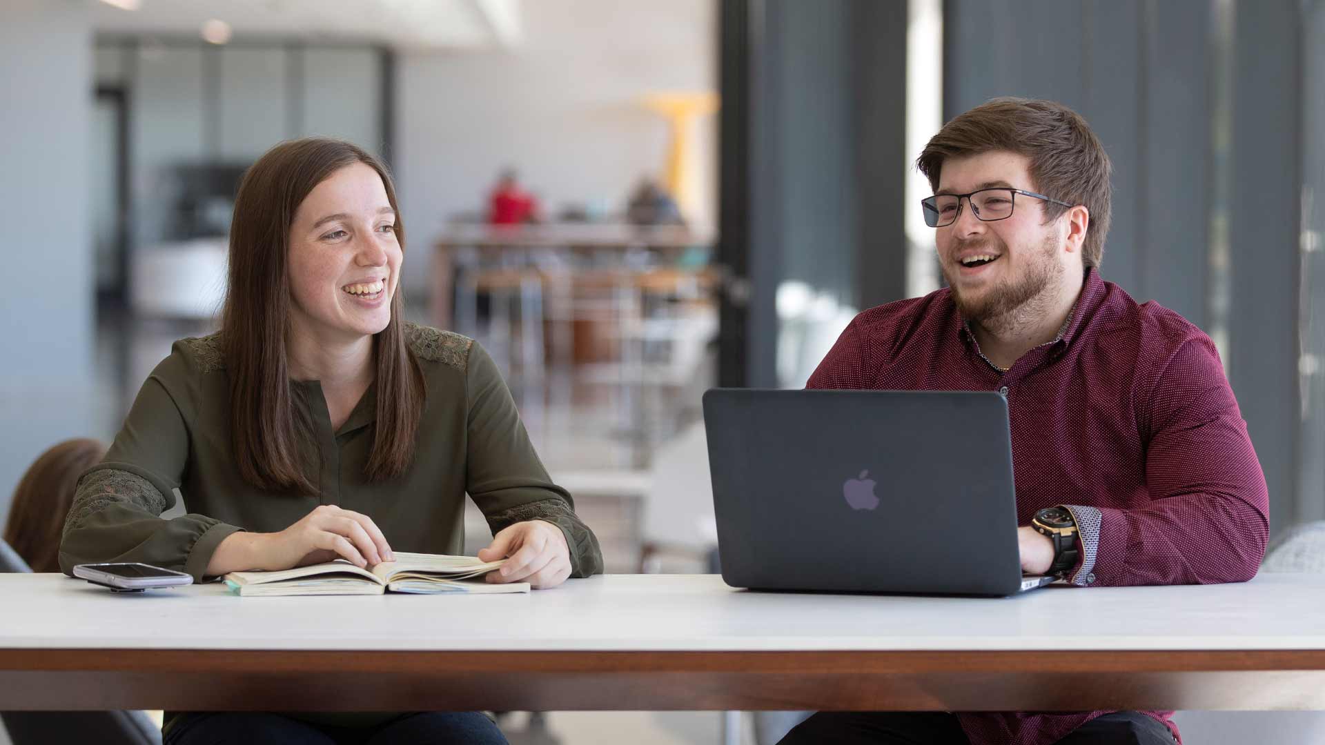 Two Missouri State students sitting at a table, within the library, smiling and talking. 